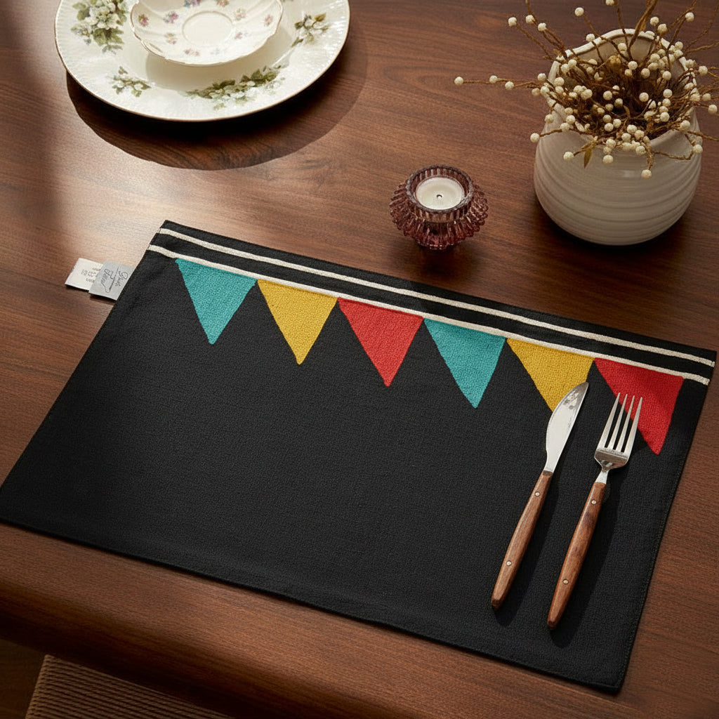 Black cotton placemat featuring red, teal, and mustard triangle embroidery in Bauhaus style
